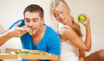En kvinne som spiser et eple ser lengselsfullt på en mann som spiser pizza