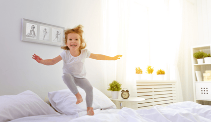 Et barn hopper gledelig på sengen med et stort smil om munnen, og demonstrerer bevegelsene som muntrer oss opp