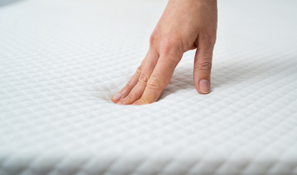 En hånd presser de tre langfingrene inn i en hvit madrass for å kjenne hvor myk den er.