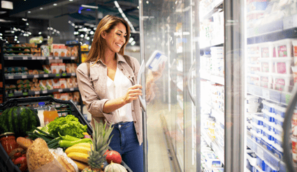 En kvinne som leser ingredienser på en dagligvarevare mens hun handler med en vogn full av sunn mat