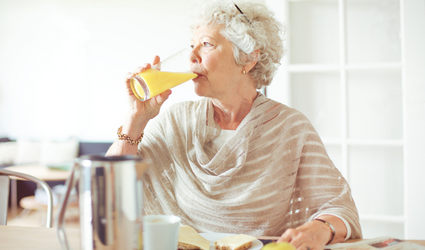 En eldre kvinne som drikker appelsinjuice til frokostmåltidet, viser at selv sunne mat og sunne drikker er best å ha til måltidet i stedet for mellom måltidene.