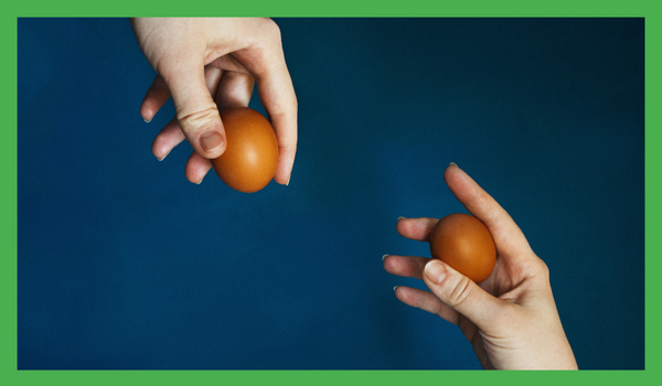 Two seprate hands holding an egg blu background